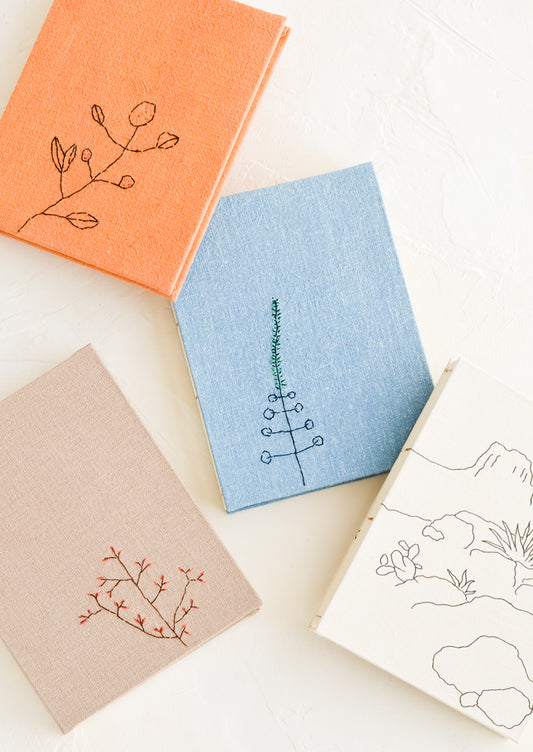 An array of cloth covered journals with botanical embroidery on covers.