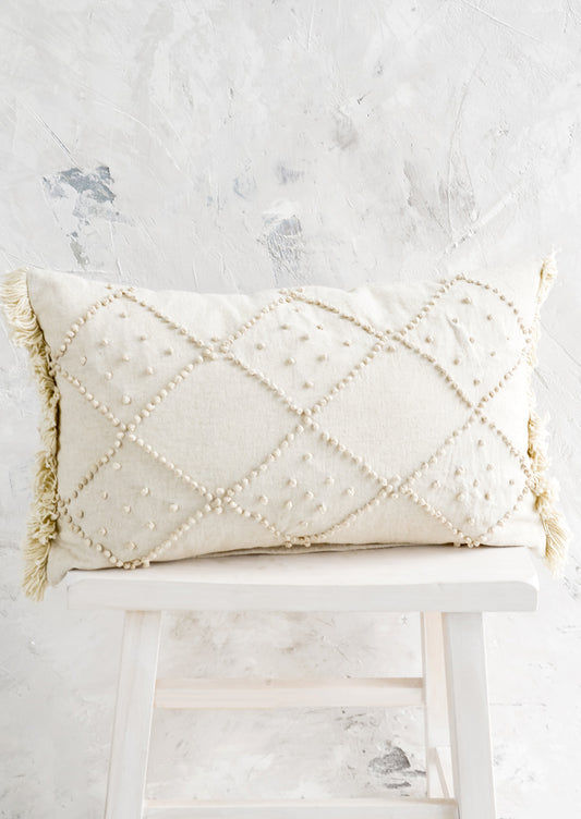 A natural cotton lumbar pillow with knotted design in diamond shape.