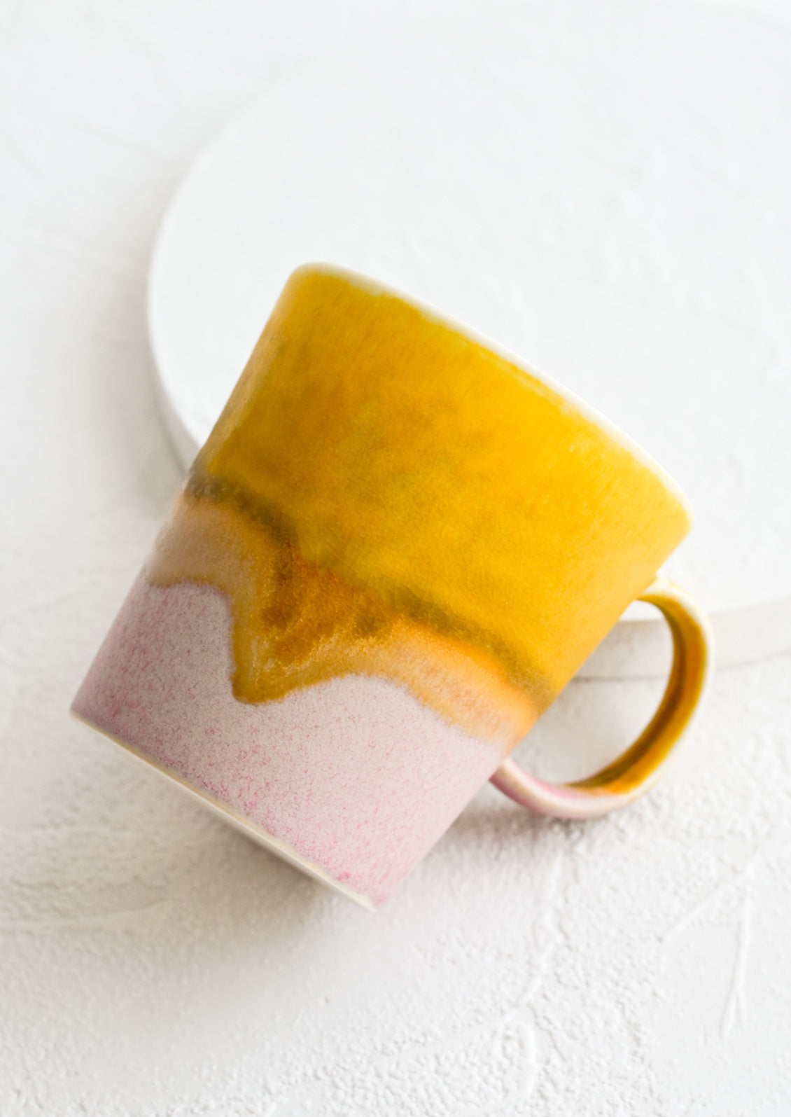 A coffee mug with a handle in mustard and light pink.