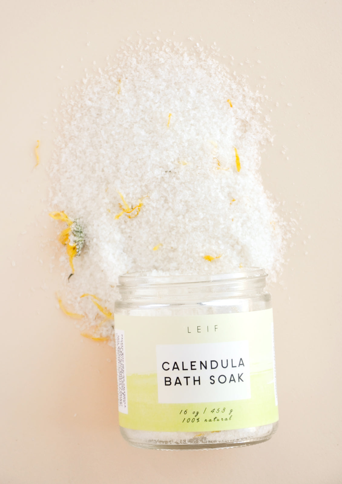 White powder with specks of yellow flowers spills out of a glass jar with a yellow-green label.