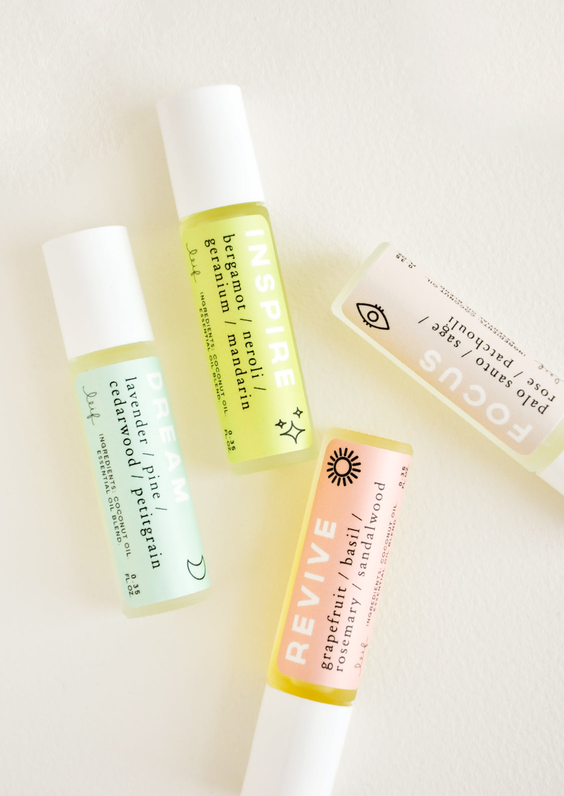 Four rollerball bottles with white caps and blue, green, peach, and purple labels