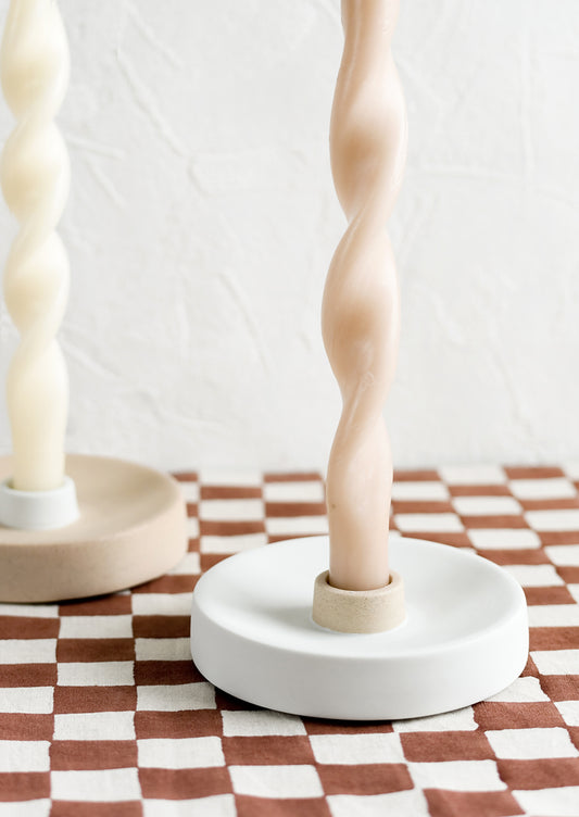Taper candles and holders on a checkered tablecloth.