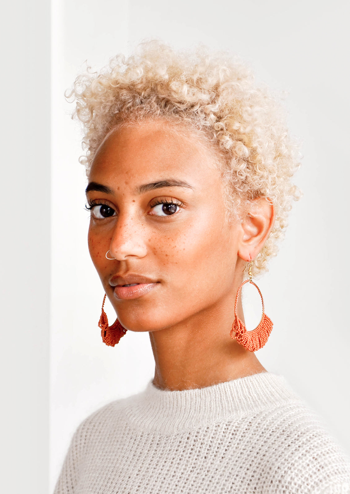 Model shot of woman wearing earrings and a white top. 