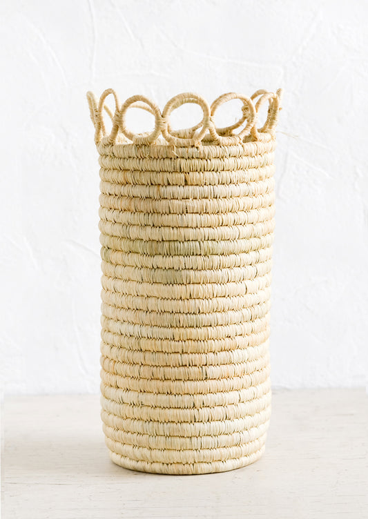 A tall, cylindrical vase in natural raffia with open circle trim along top.