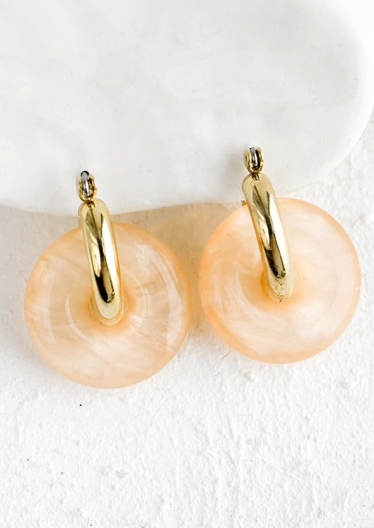 A pair of peach resin donut shaped charms on gold hoop earrings.
