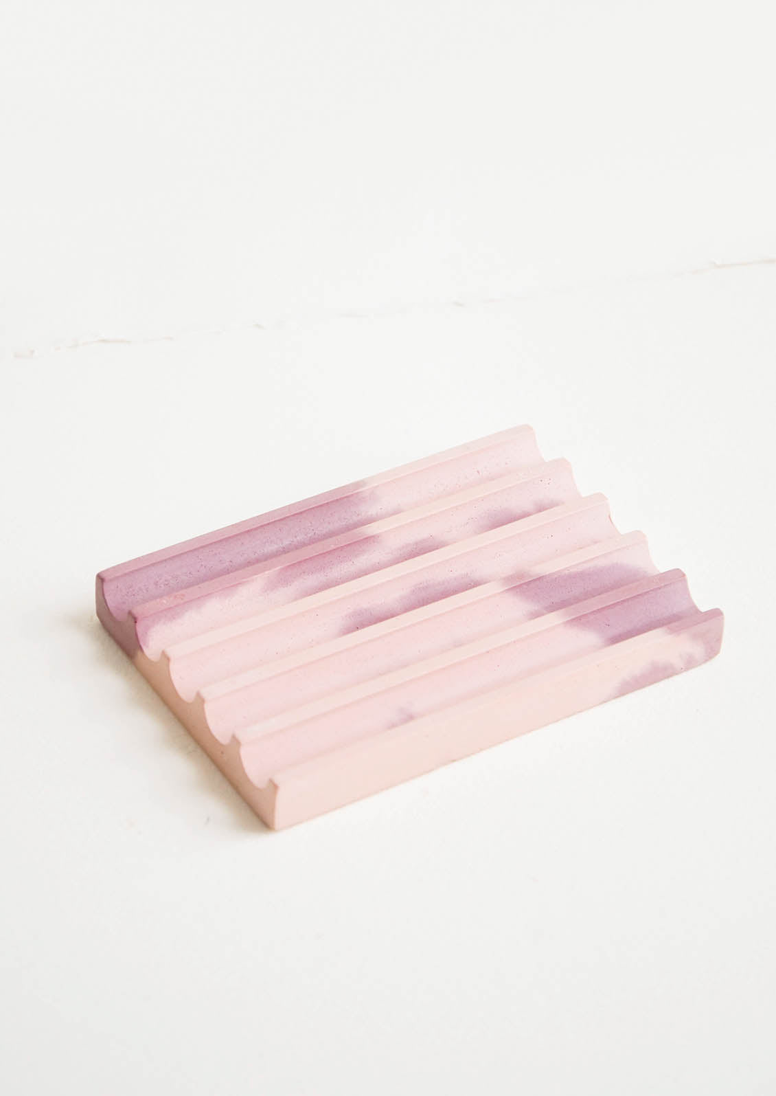 A marbled pale pink and mauve smooth concrete soap dish with troughs and ridges.