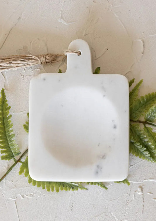 A paddle shaped spoon rest with center well in white marble.