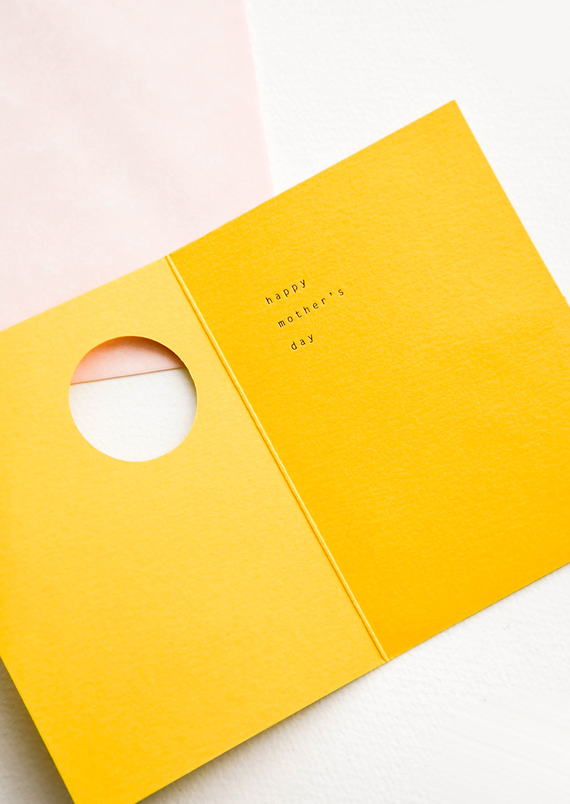 Yellow greeting card featuring circular cut out on front, revealing an interior message