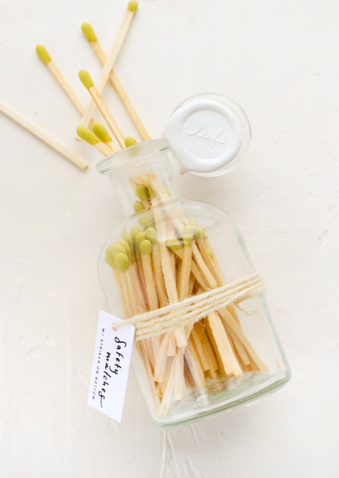 Safety matches with lime green tips in a vintage-style glass apothecary jar with white wax seal on lid.