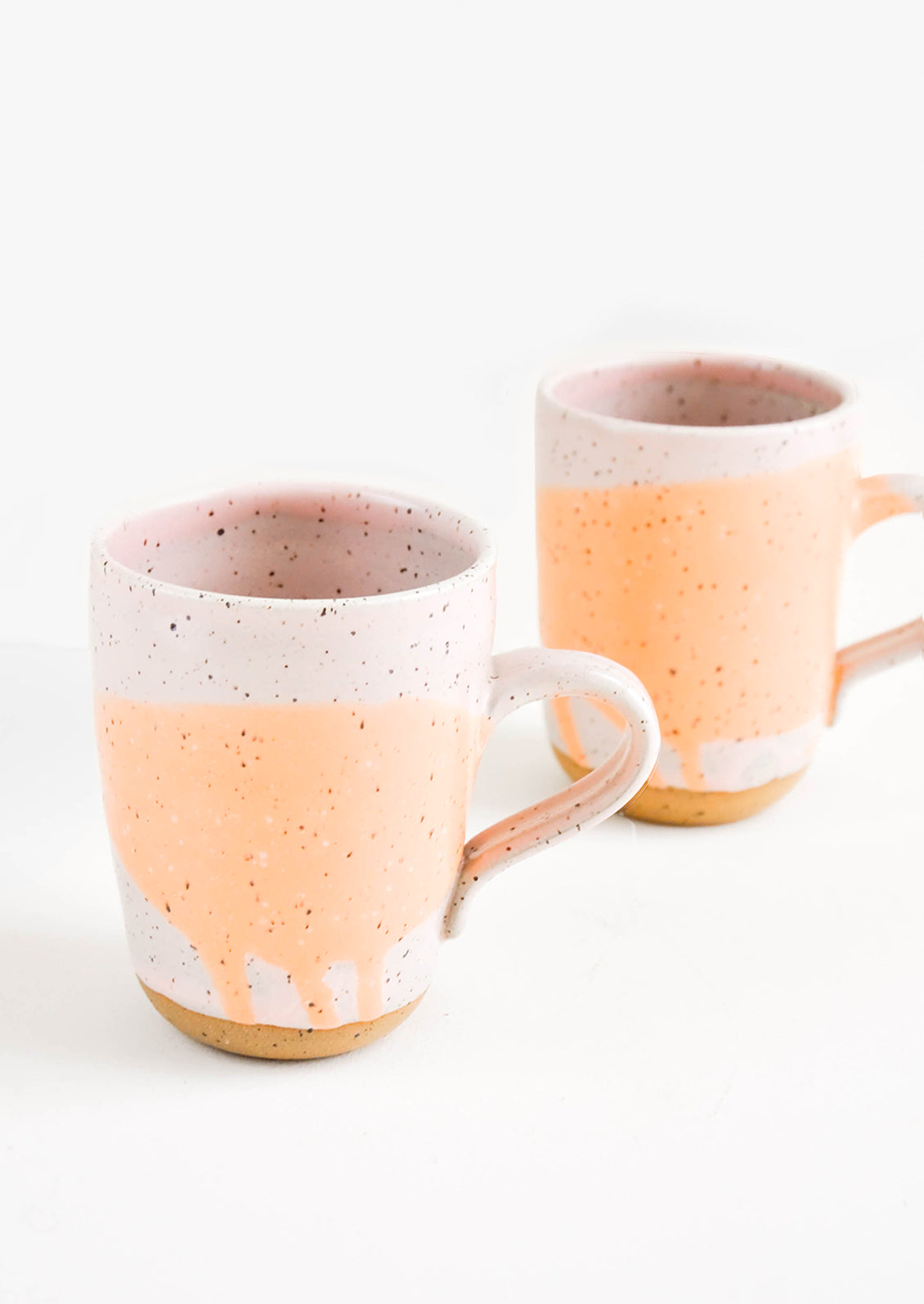 Two ceramic mugs in orange and pink with brown speckles.