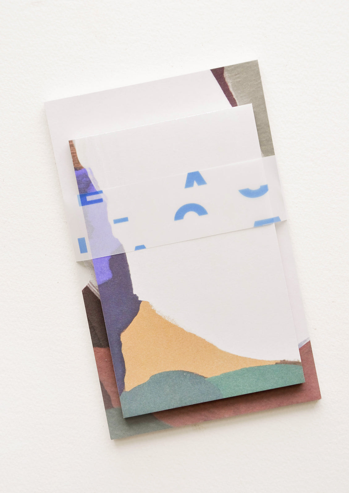 Two stacked notepads wrapped with cellophane, decorated with colorful abstract shapes.