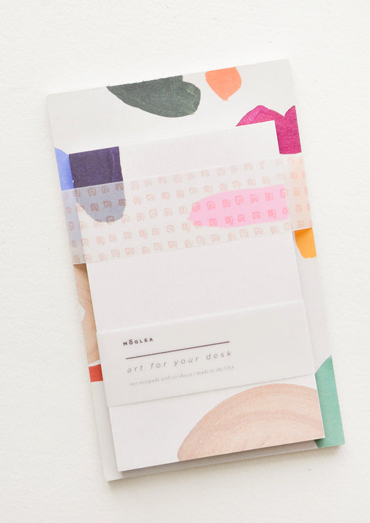 Two stacked notepads wrapped with cellophane, decorated with colorful abstract shapes.