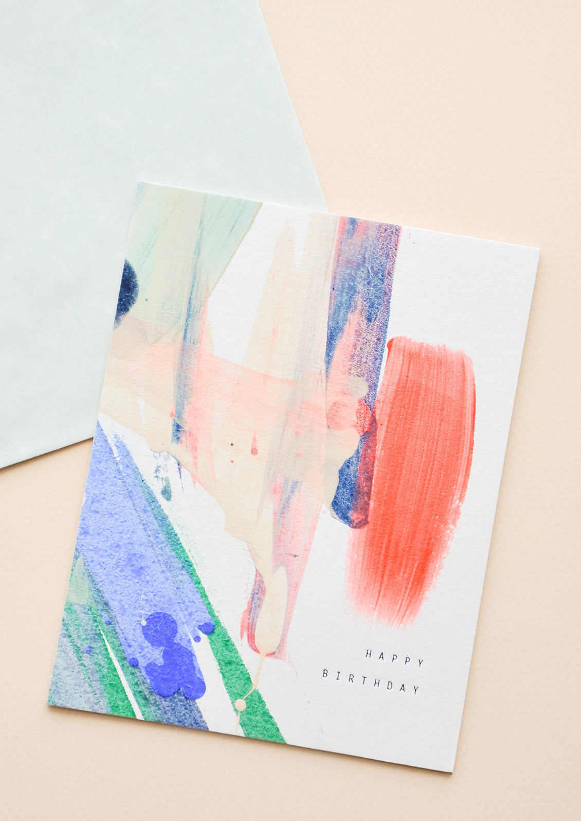 Notecard with watercolor painted abstract decoration and the text "Happy Birthday" with green envelope.