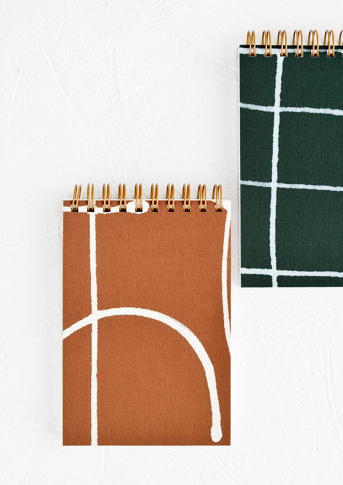 Small pocket sized, spiral bound notebooks in green and brown.