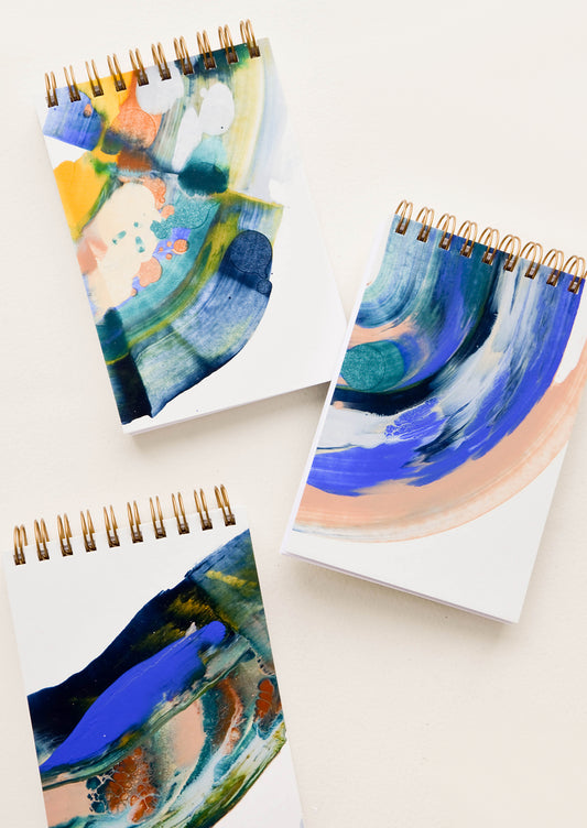 Small, pocket-size spiral notepads with covers painted in earth toned paint swirls