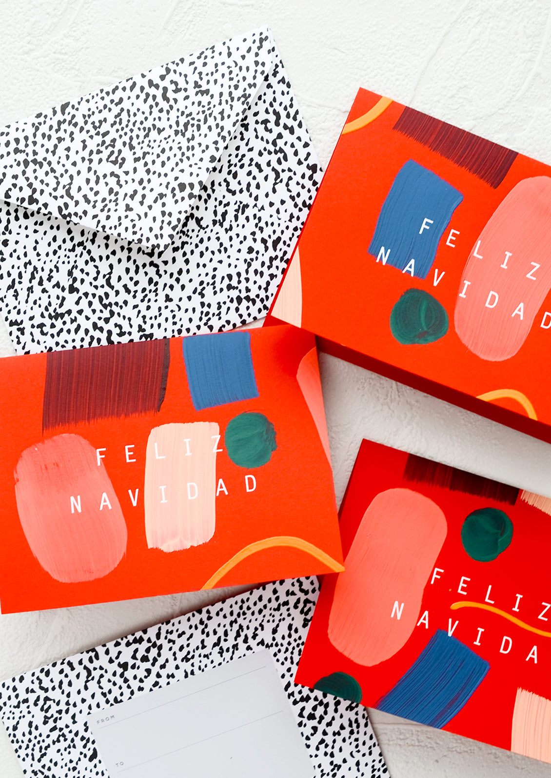 Three greeting cards in red with hand painted geometric shapes and "Feliz Navidad" printed in white letters.