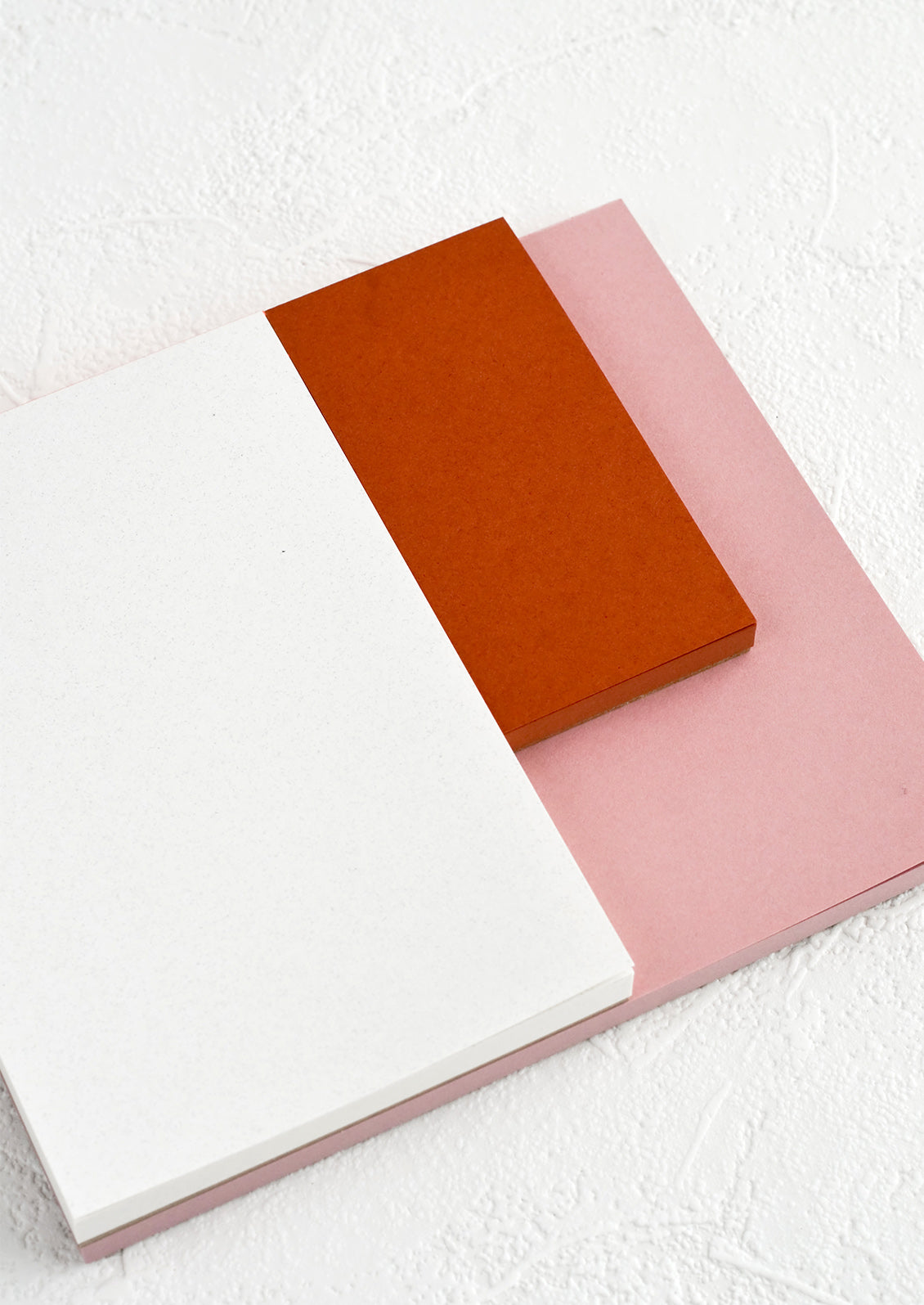 A landscape oriented notepad with three separate sized sections in different colors.