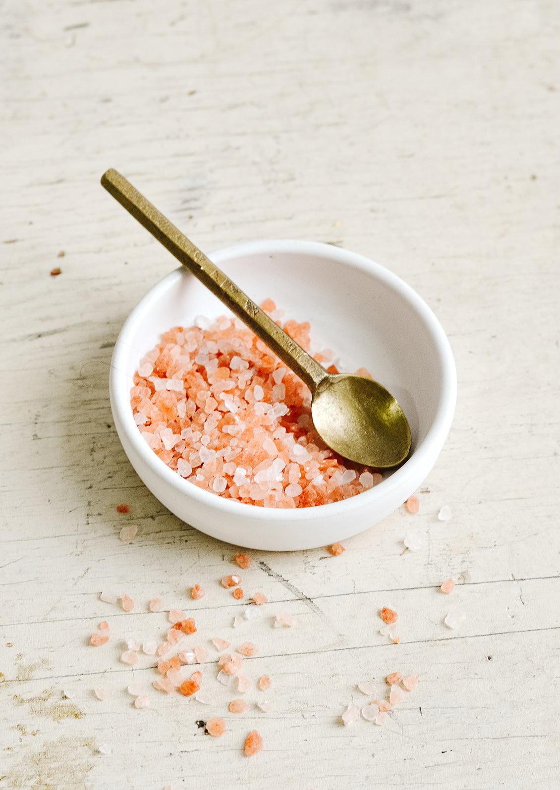 A brass spoon inside a small white dish with coarse pink salt.