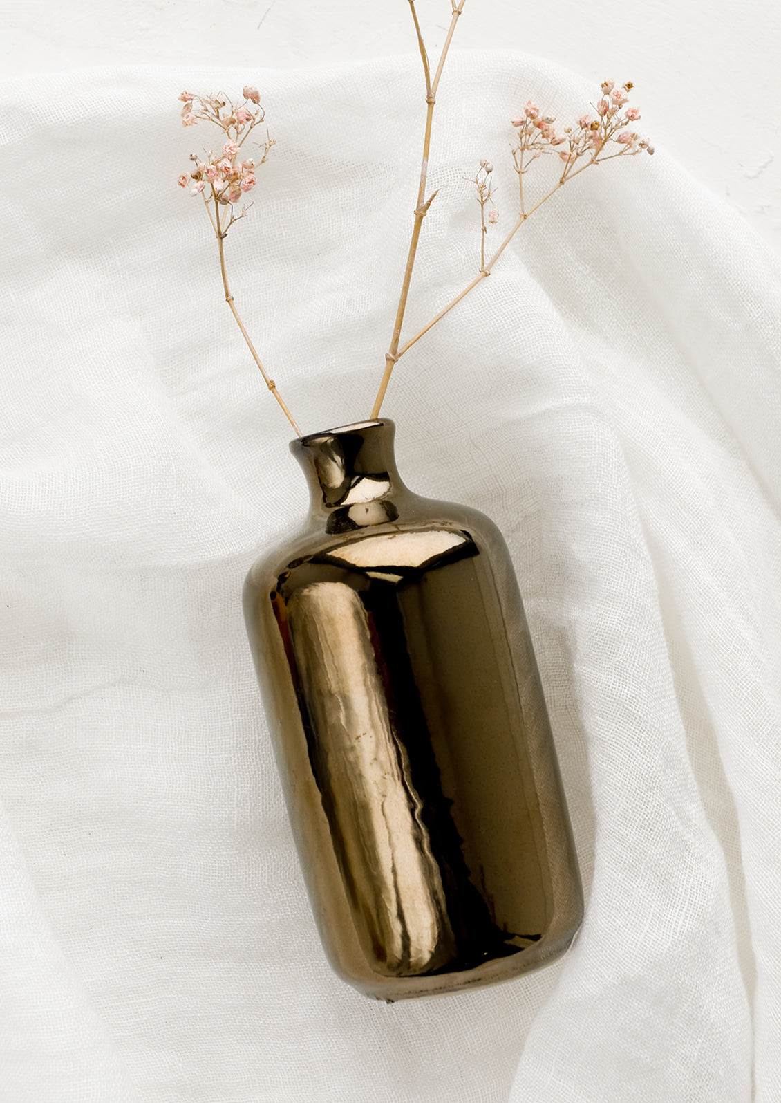 A ceramic bud vase in tall shape, bronze color with dried flower.