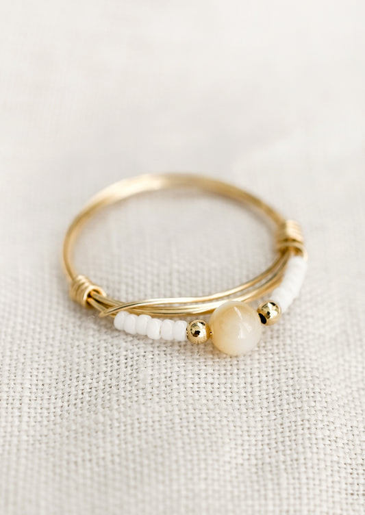 A gold wire ring with white and tan beads.