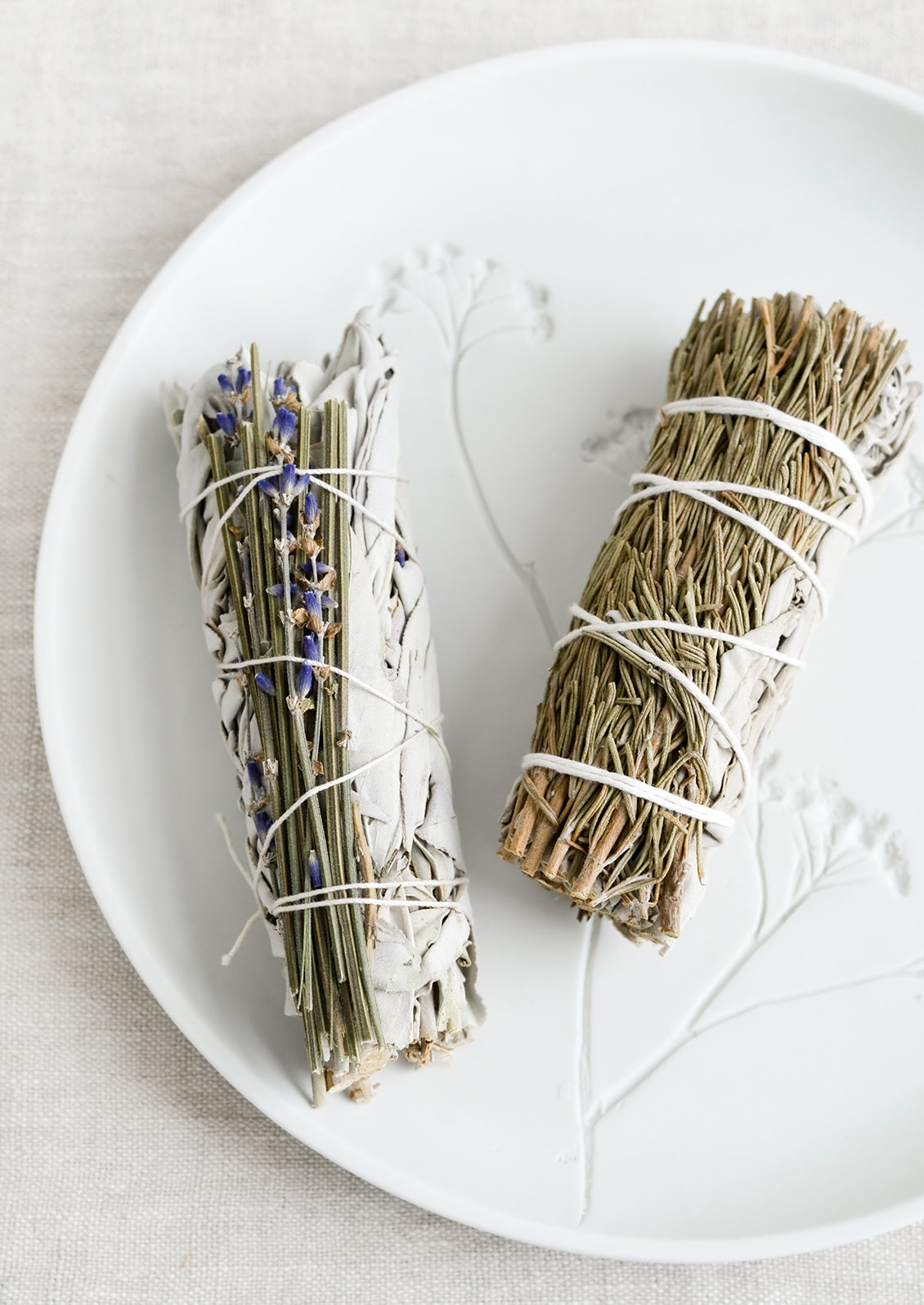 Two sage smudge sticks on a ceramic plate.