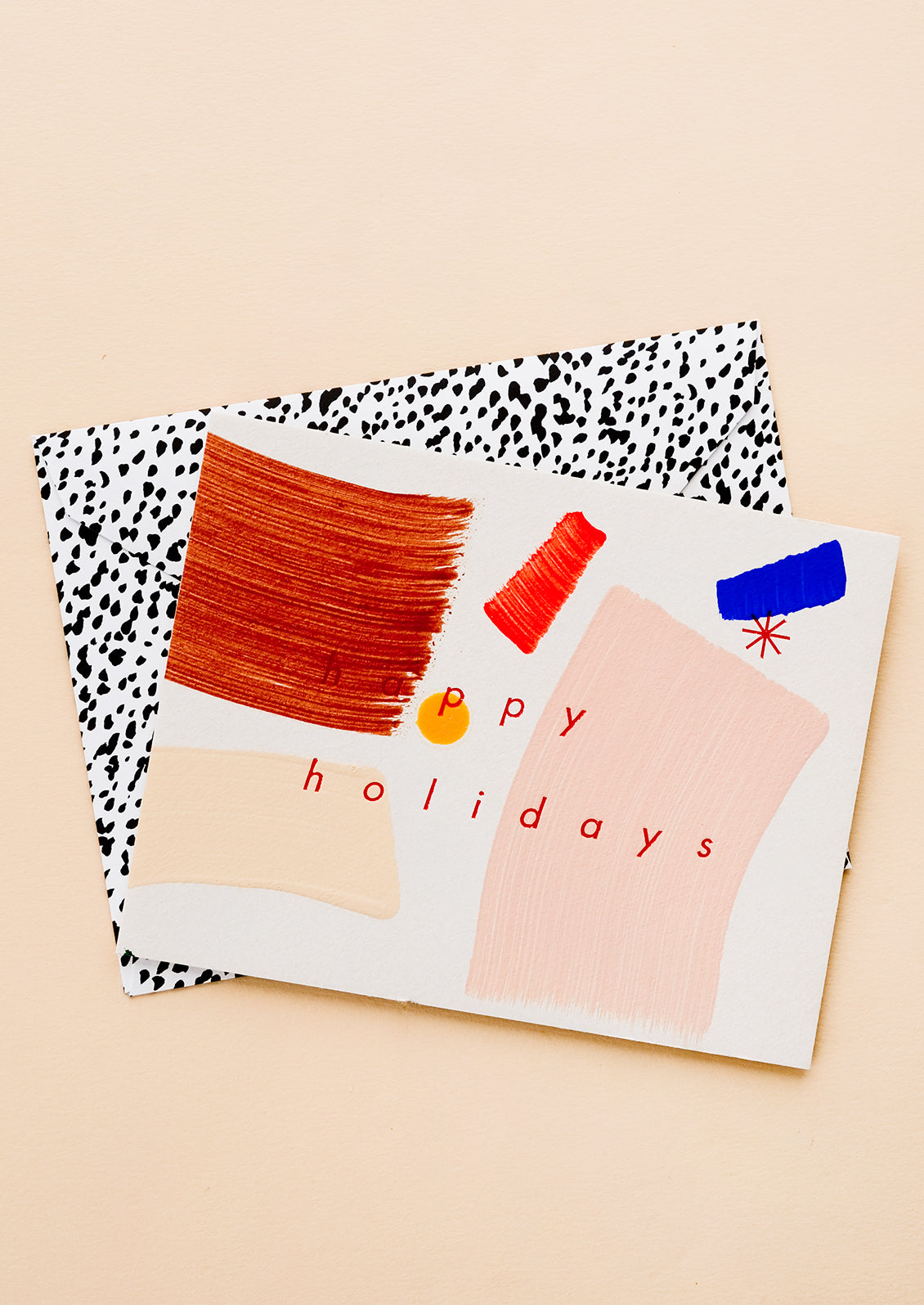 A greeting card with hand-painted brushstrokes and "happy holidays" in red lettering, and a black and white patterned envelope.