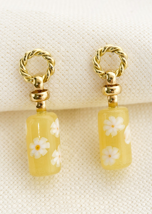 A pair of earrings with circular braided brass post and yellow floral glass bead.