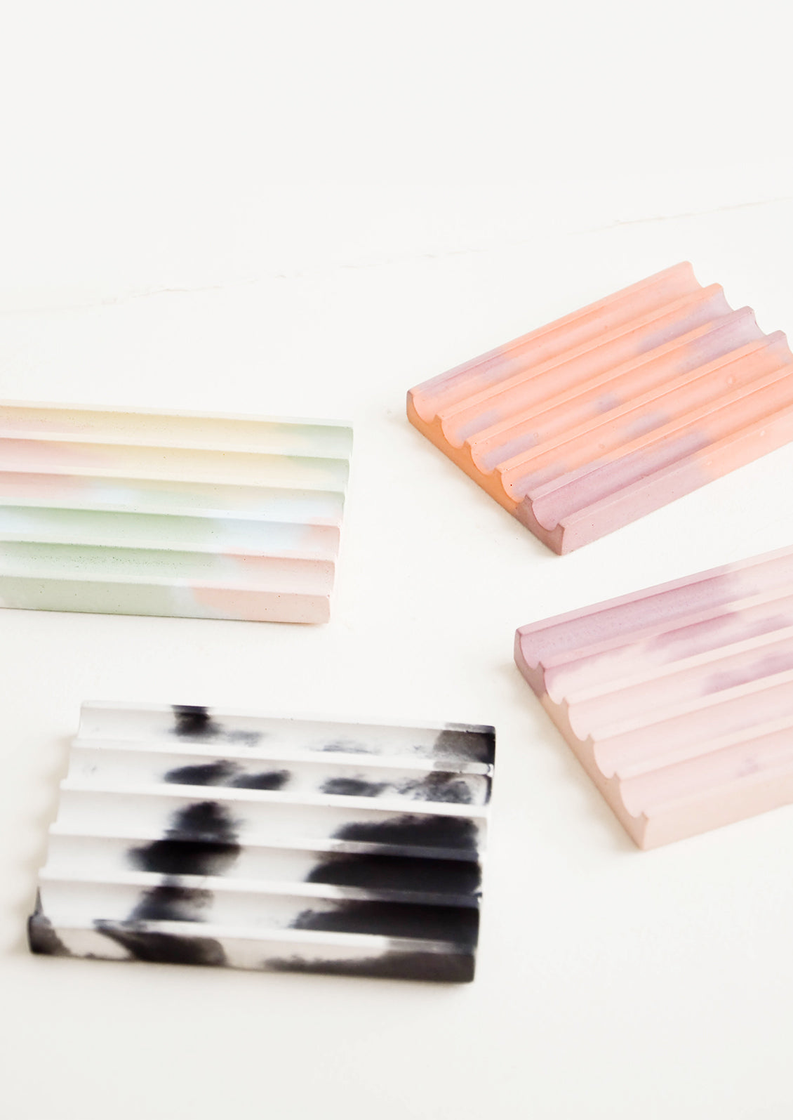 Four smooth concrete ridged soap dishes in rainbow, coral, pink, and black and white.
