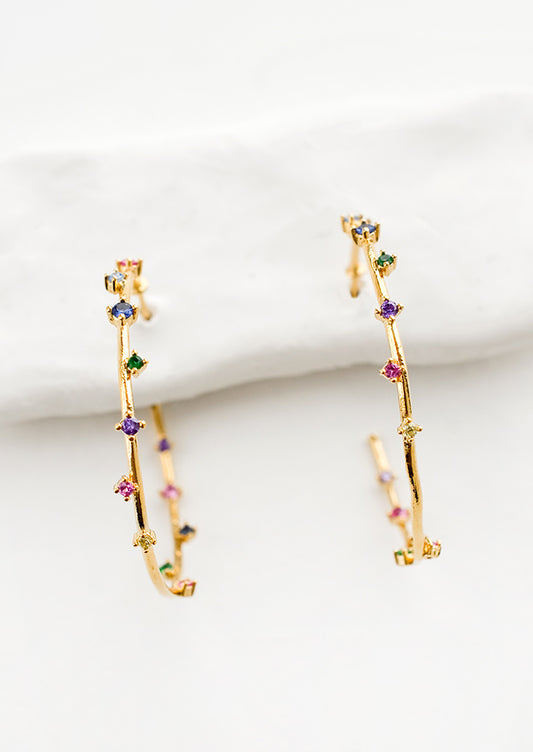 A pair of gold hoop earrings with colored crystals wrapping around the hoop sporadically.