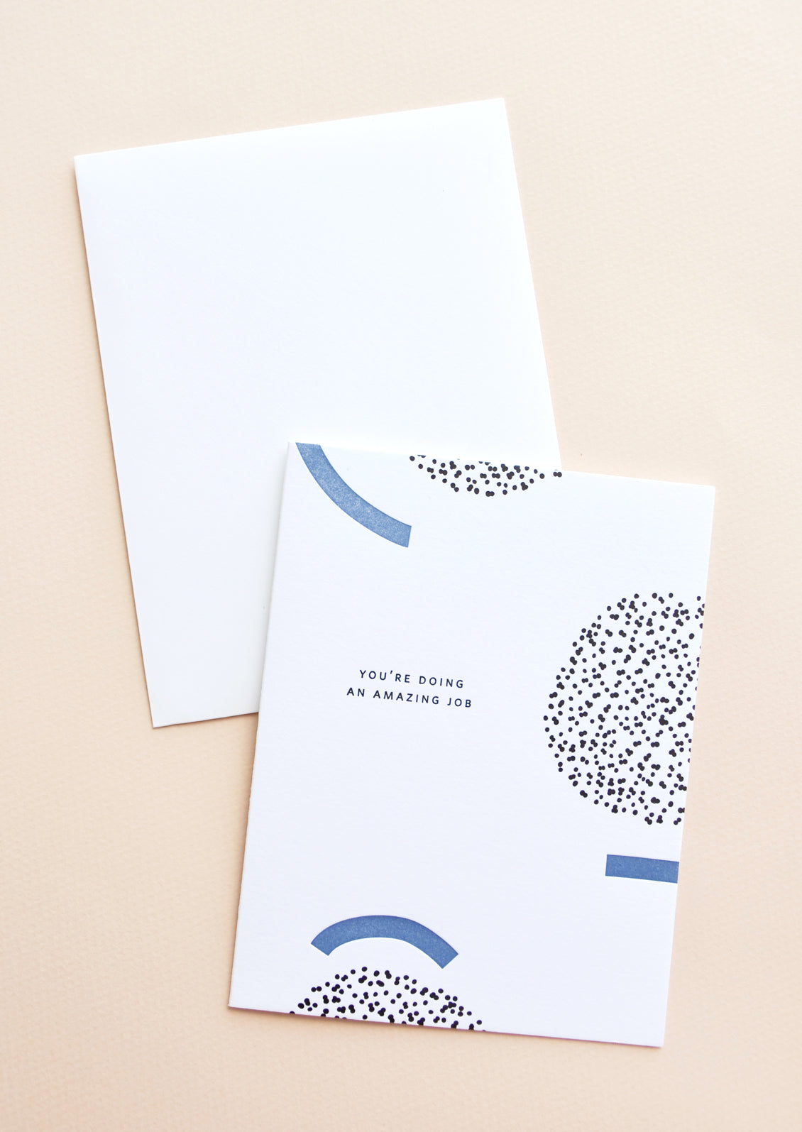 White notecard with black and blue geometric decoration and the text "You're doing an amazing job", with white envelope.