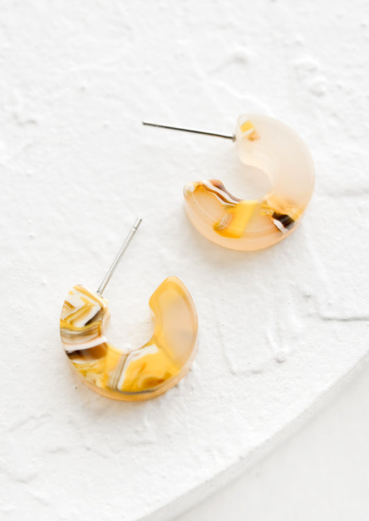 A pair of small acetate hoop earrings in marbled yellow color.
