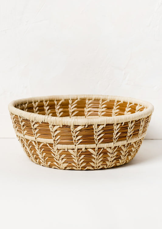 A woven catchall basket in bowl shape made from pine needles and raffia.