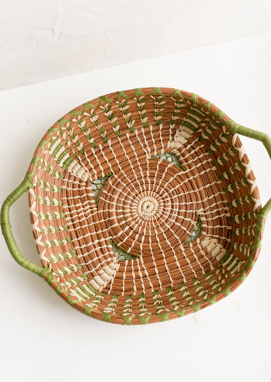 A shallow basket in rounded square shape with rectangular green handles at sides.