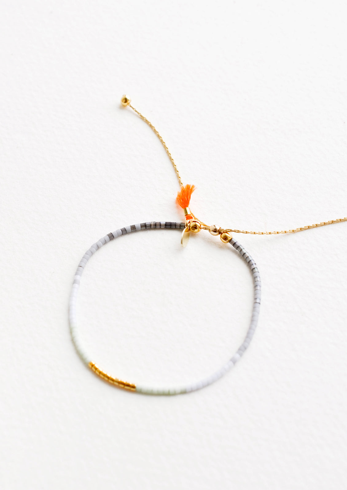 Delicate bracelet of glass beads in a gradient of deep gray to pale blue with gold beads at center on a thin gold chain.