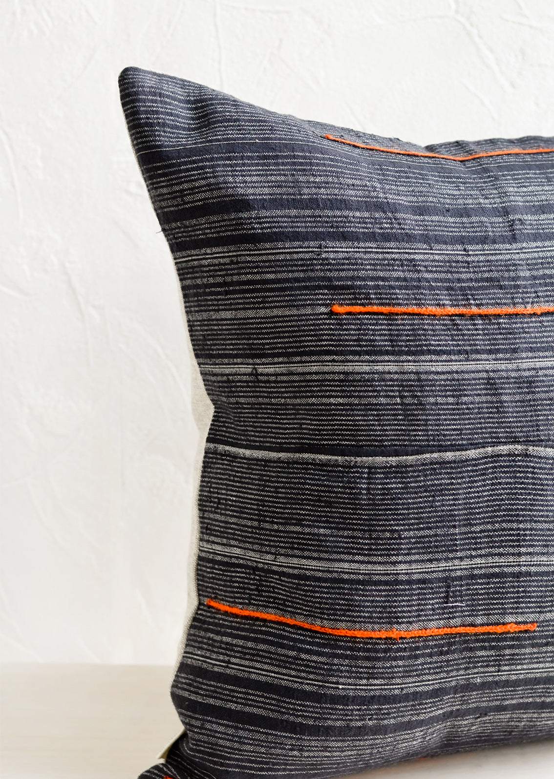 A square throw pillow made from dark blue fabric with grey stripes and embroidered orange lines.