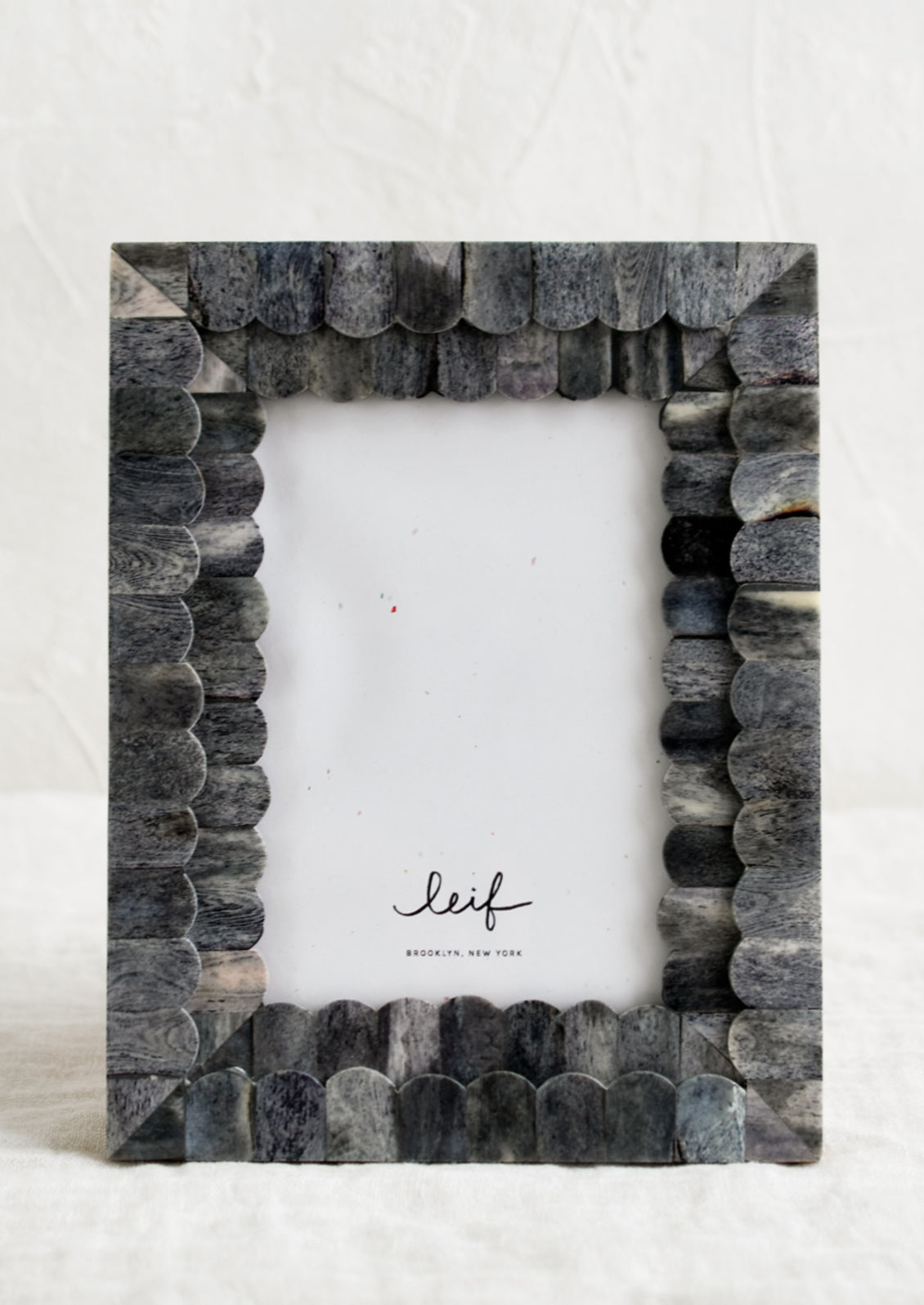 A tabletop picture frame with scalloped grey bone border.