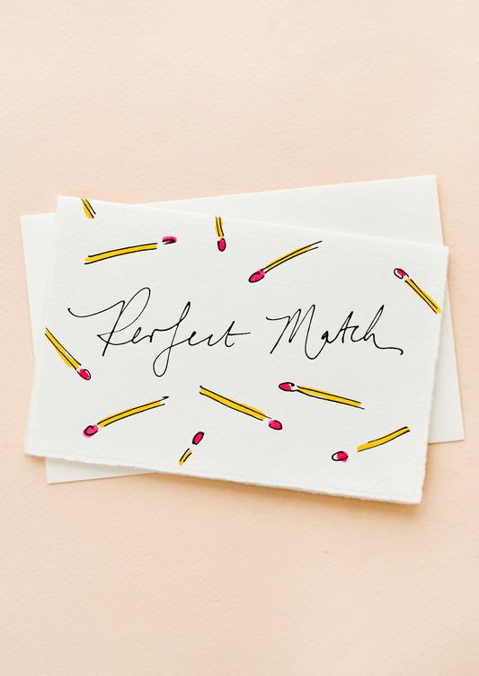 A white greeting card with hand-painted match sticks and "Perfect Match" written in cursive.