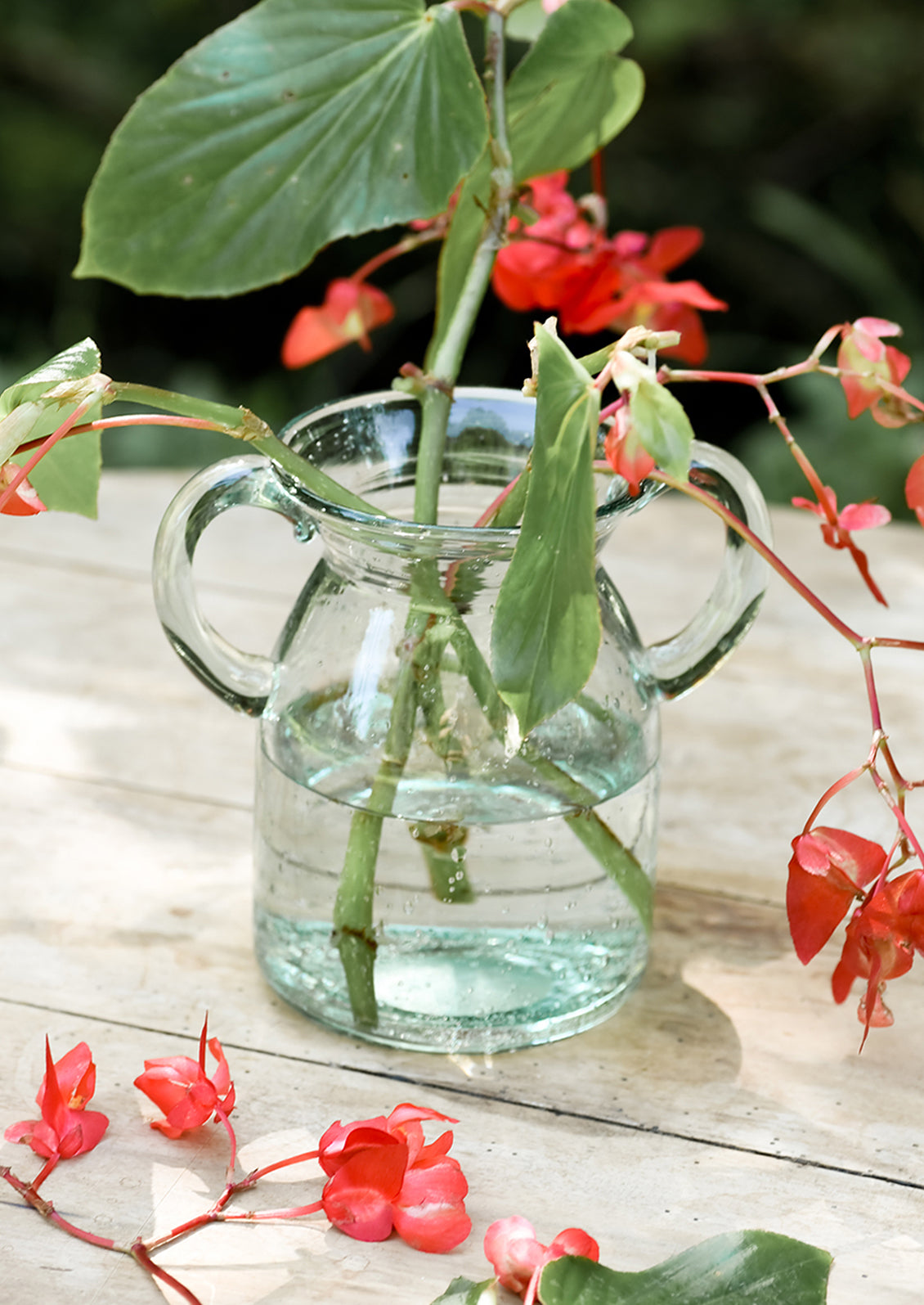 A clear, jug-shaped glass vase on a table with flowers.