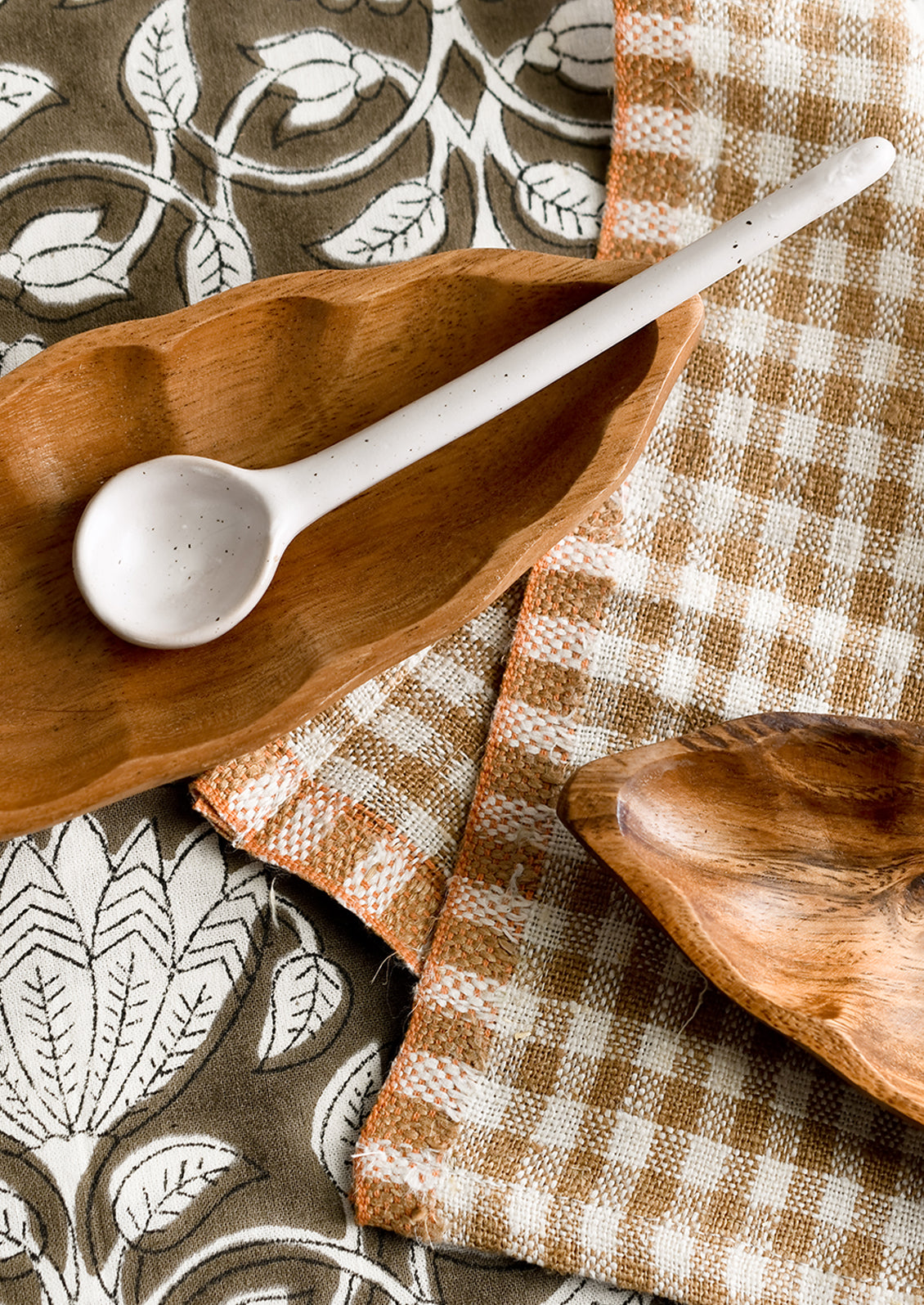 Styled scene with spoon, wooden dishes and table textiles.
