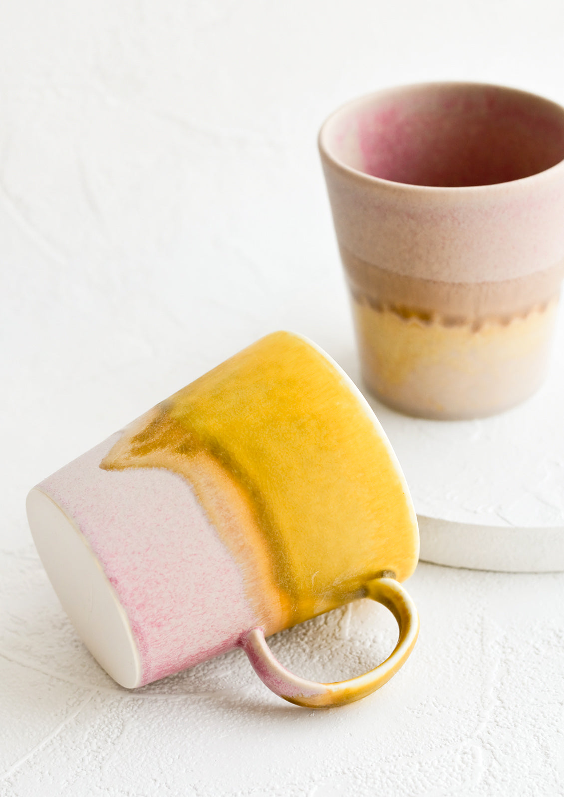 Ceramic coffee mugs in pink, yellow and brown tones.