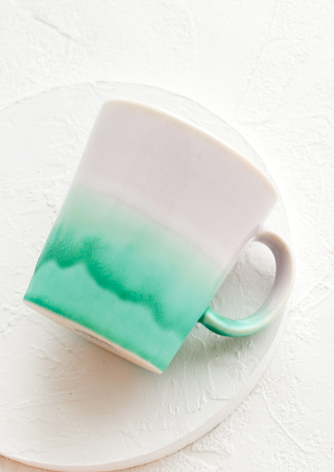 A ceramic coffee mug with handle in lavender and sea green glaze.