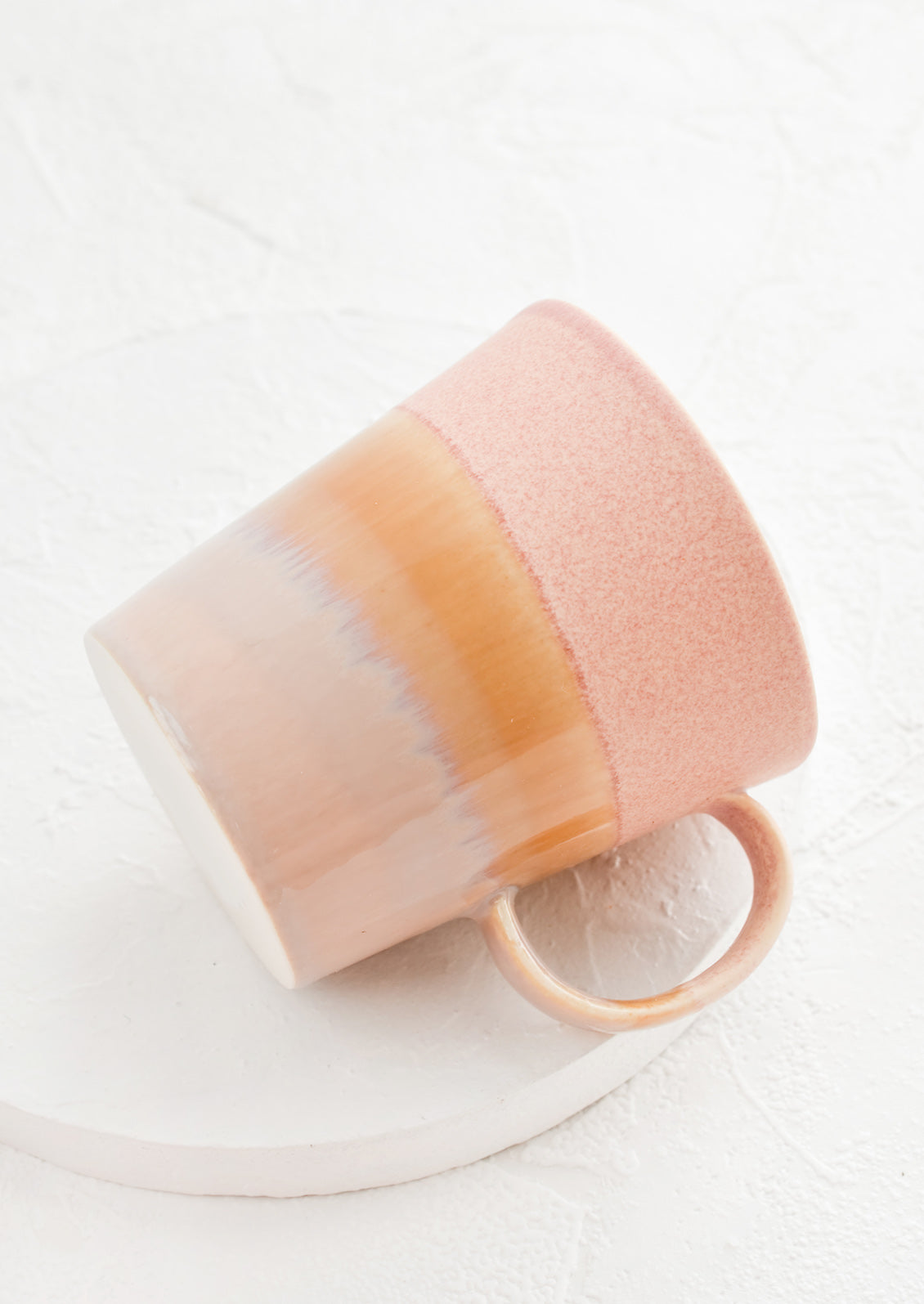 A coffee mug with a handle in pink, yellow and brown.