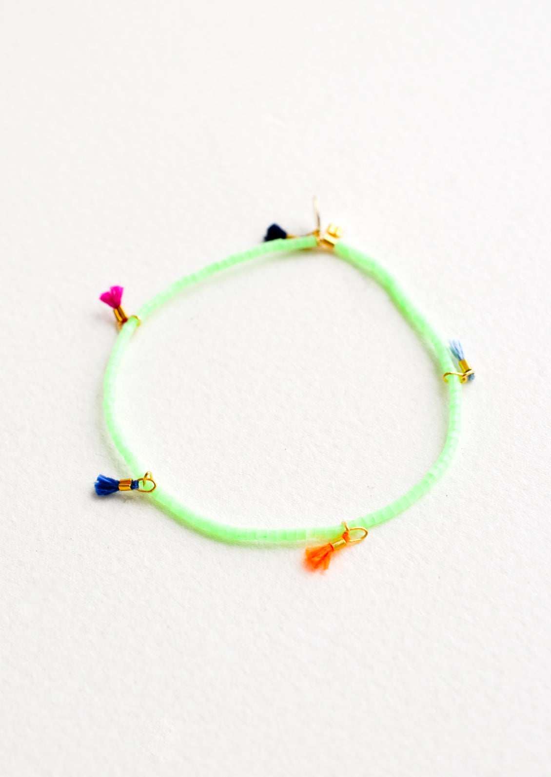 Bracelet featuring green beads interspersed with 5 small multicolor string tassels on an elastic cord.