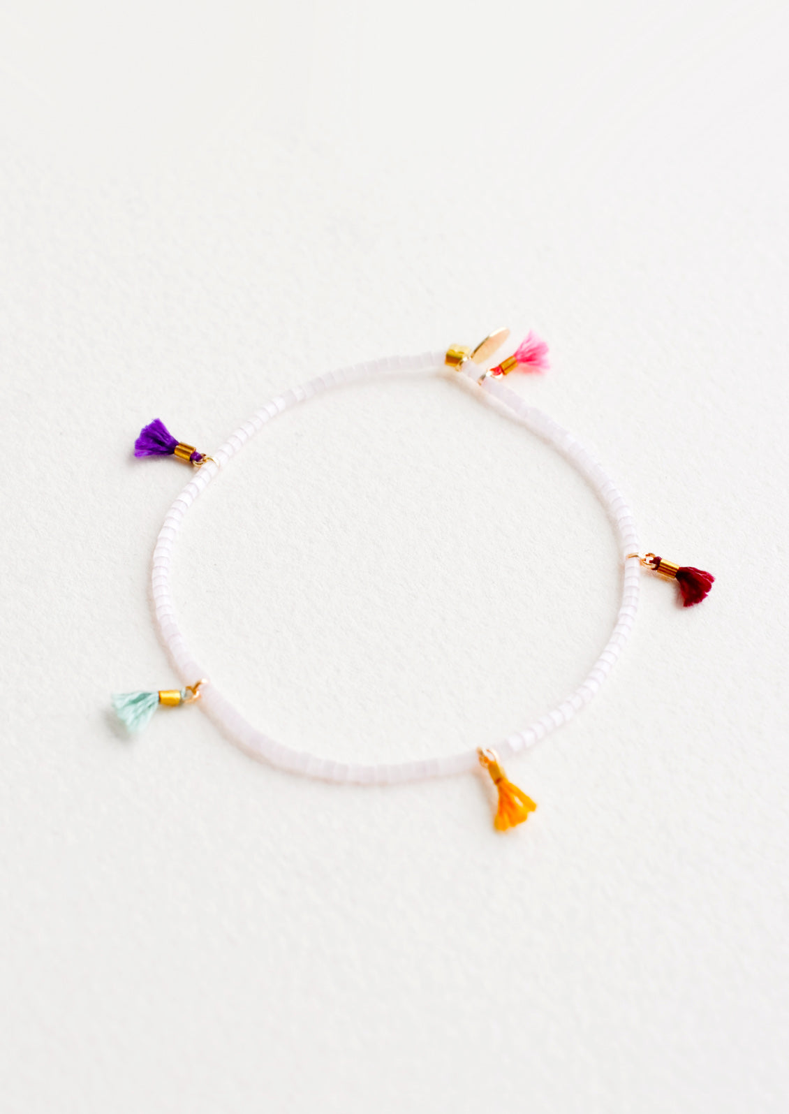 Bracelet featuring white beads interspersed with 5 small multicolor string tassels on an elastic cord.