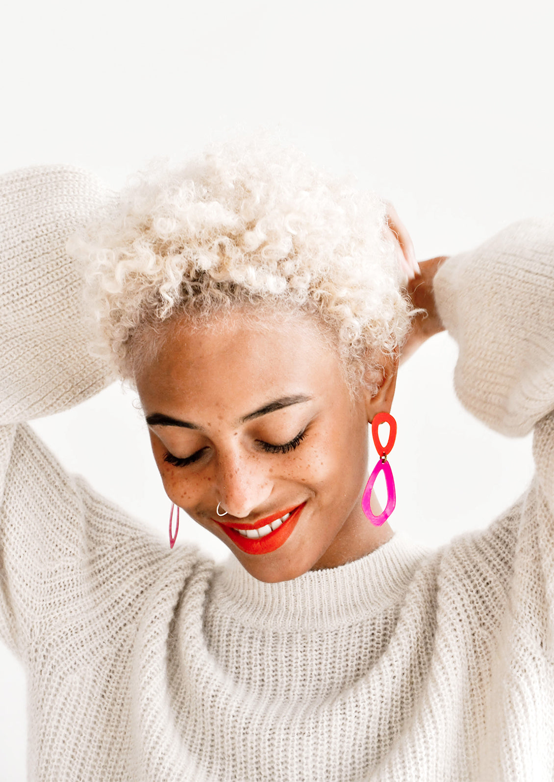 Model wears vibrant coral and fuchsia drop earrings and ivory sweater.