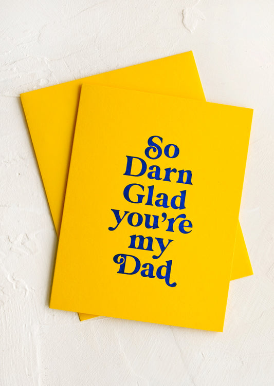 A yellow greeting card and yellow envelope, card reads "So darn glad you're my dad" on front.