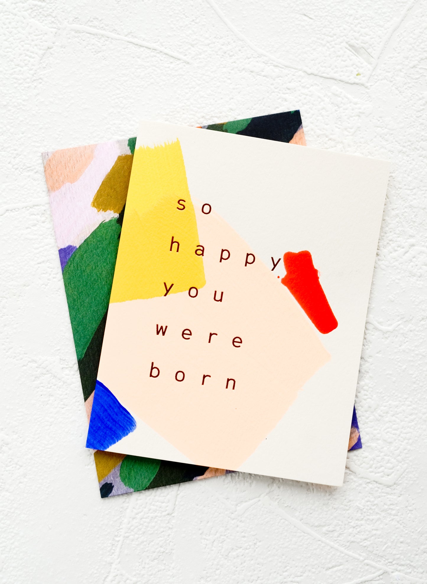 A greeting card with hand-painted geometric shapes and text reading "So happy you were born"