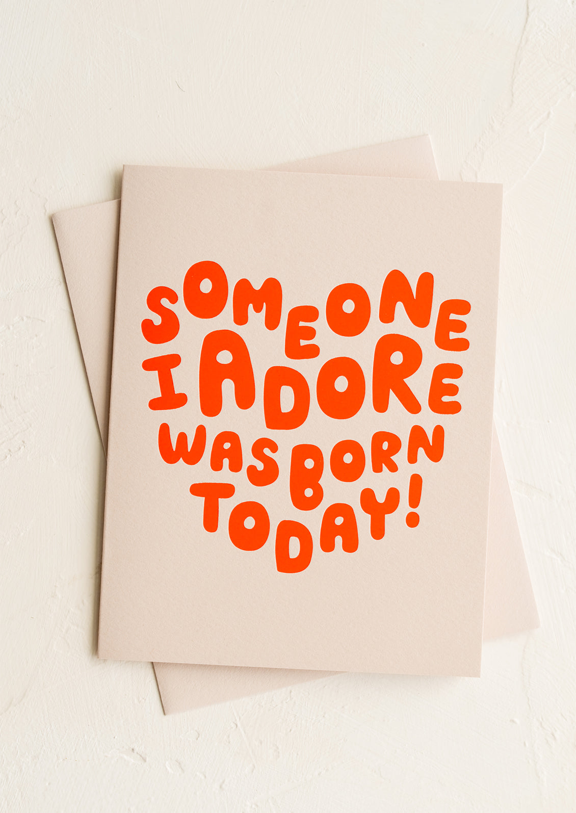 A tan greeting card with red letters in heart shape.