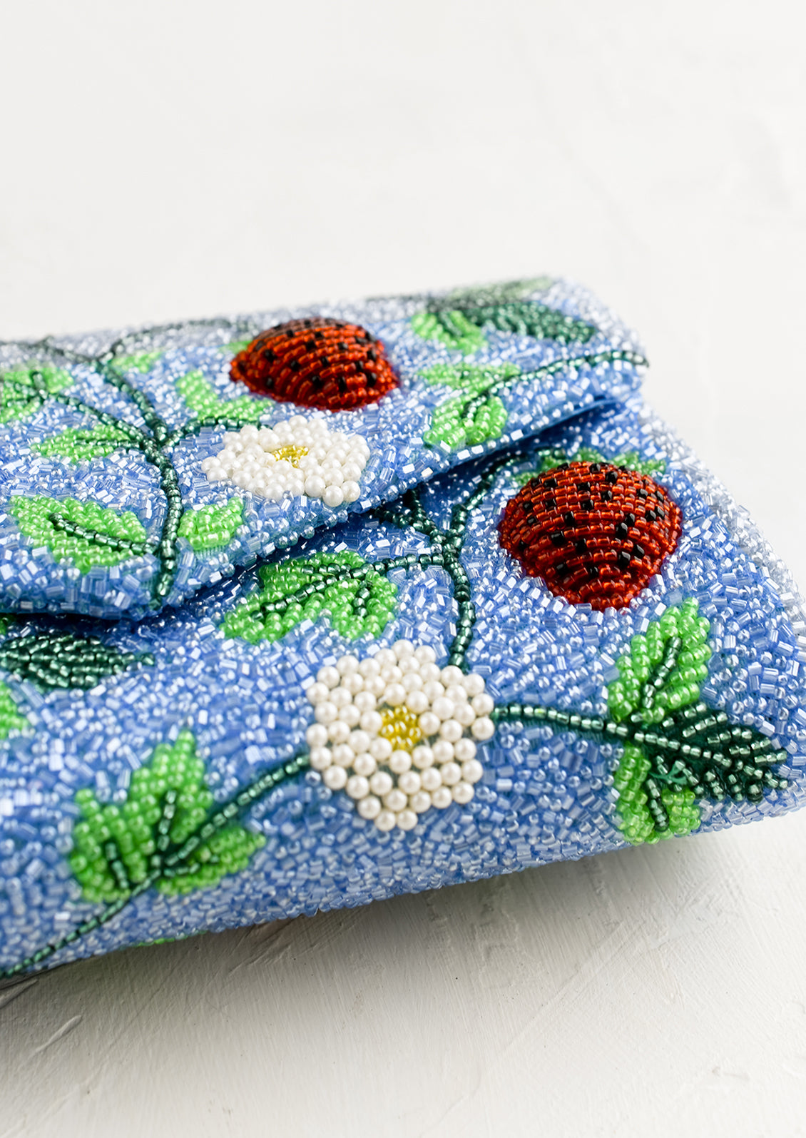 A blue beaded clutch with red strawberry pattern.