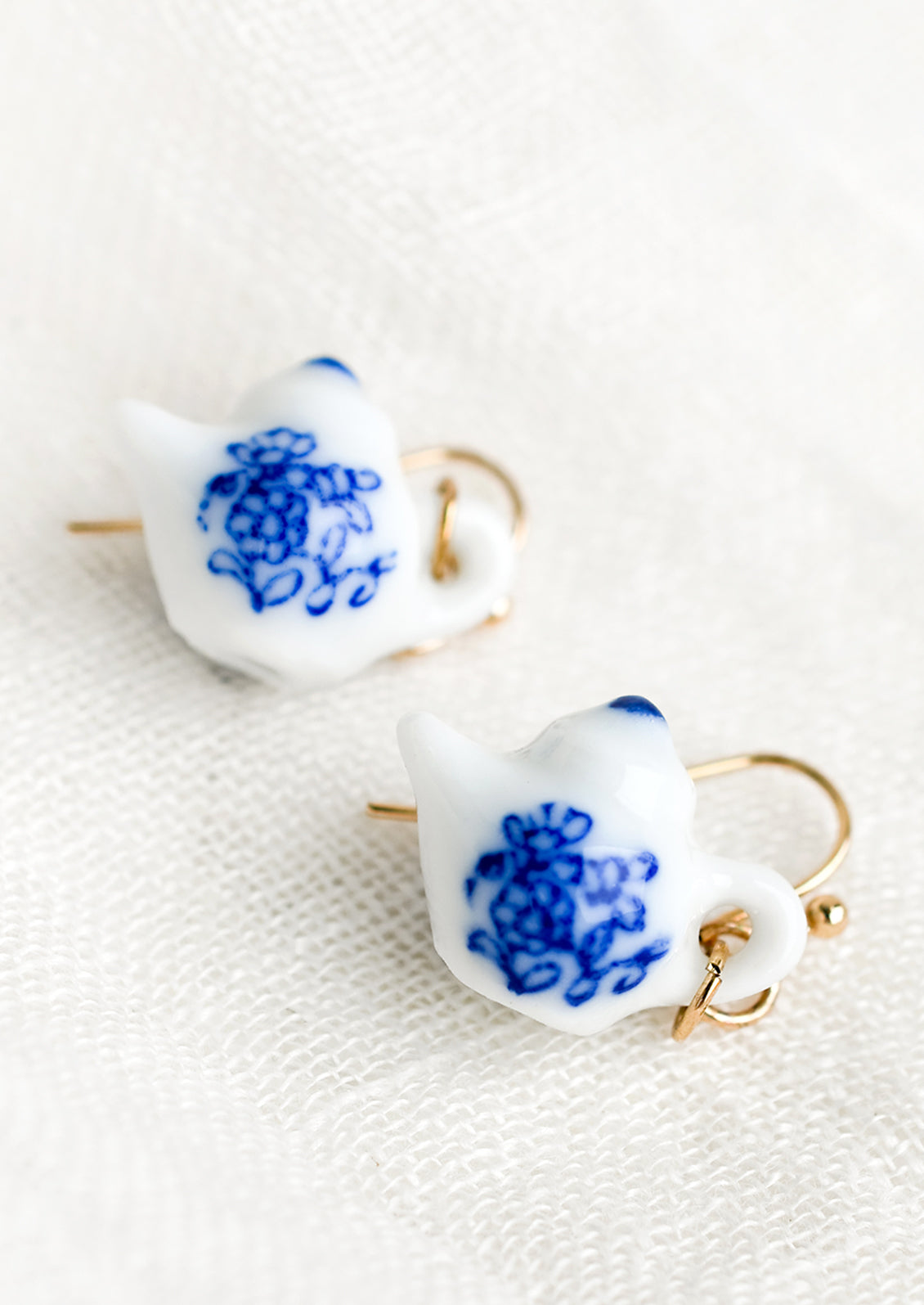 A pair of earrings in shape of white teapot with blue floral print.